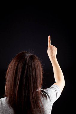 Uzun kahverengi saçlı, koyu arka planda kısa kollu gömlek giyen beyaz bir kadının kafasının arkasında. İşaret parmağıyla işaret ediyor gibi. Bir numara için kavram.