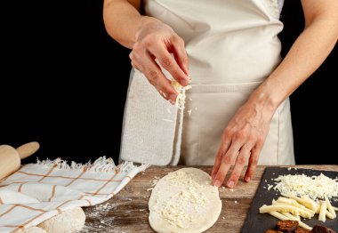 Ahşap mutfak tezgahında düz bir hamur. Ekmek, ekmek, peynir ve sümüklü ekmeklerle konsept bir görüntü oluşturuyor. Türk kasarli berbat pide tarifi. Bir aşçı dilimlenmiş peynir serpiyor..