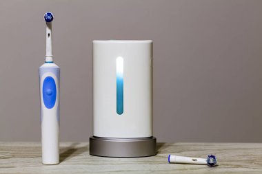 Close up isolated image of an ultraviolet toothbrush head sterilizer device that is working in the middle with electric toothbrush on the left an a spare brush head on the right on bathroom counter.