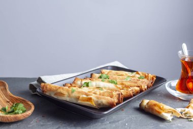 Traditional Turkish sigara boregi, a phyllo dough roll with cheese or ground meat stuffing. Deep fried rolls are served on a tray with parsley leaves as topping and Turkish tea on the side.
