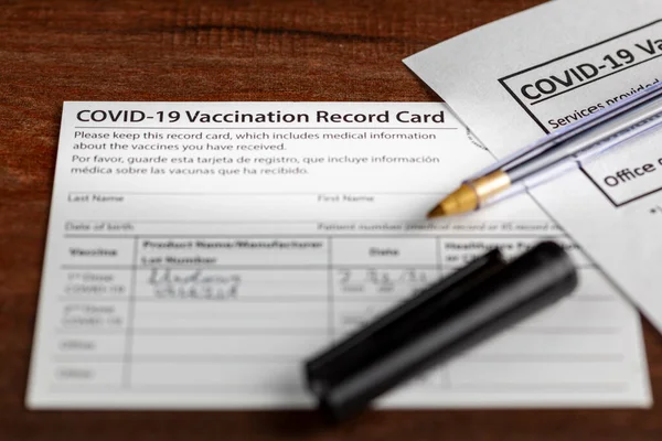 Close up isolated image of a COVID 19 vaccination record card on a wooden desk. The card details the date, type and the dose number of administered vaccine and given to every person for record.