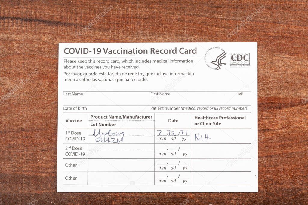 Bethesda, MD, USA 03-22-2021: a COVID 19 vaccination record card on a wooden desk. The card details the date, type and the dose number of administred vaccine and given to every person for record.
