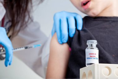 Çocuklar arasında COVID 19 aşısının güvenliği ve etkinliği için klinik deneyler devam ediyor. Bir çocuğun kas içi enjeksiyon yoluyla COVID aşısı yaptırdığını gösteren bir konsept resim.