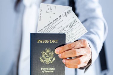 Clarksburg, MD, ABD 03-29-2021: Beyaz bir iş kadını, aşılama belgesi olarak ABD pasaportu, uçuş kartı ve COVID aşı belgesini de içeren seyahat belgelerini havaalanında gösteriyor.