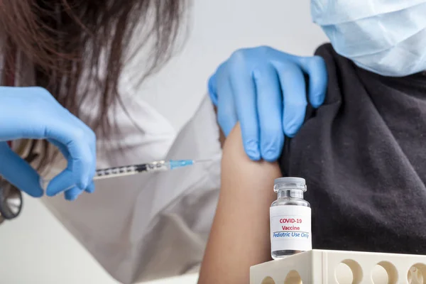 Çocuklar arasında COVID 19 aşısının güvenliği ve etkinliği için klinik deneyler devam ediyor. Bir çocuğun kas içi enjeksiyon yoluyla COVID aşısı yaptırdığını gösteren bir konsept resim.