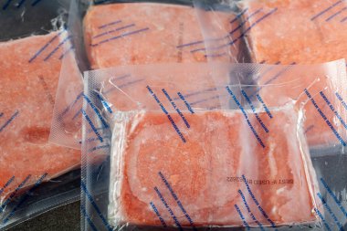 Dört paket somon fileto balığının yakın çekim görüntüsü. Hava geçirmez vakumlu paketler donmuş ve talimatlar buzlukta çözülmeleri gerektiğini söylüyor..