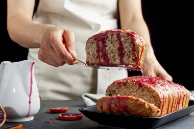 Taze ev yapımı portakallı kekin yakın plan görüntüsü somun tavada yapılmış ve koyu taş arka planda siyah porselen tabakta servis edilmiş. İçinde kan portakal suyu var..