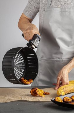 Beyaz bir kadın taze yapılmış muz cipslerini (Platanos Maduros) soğutmak için pişirme kağıdına döküyor. Kızartma sepetinin sapını tutuyor. Kızartma makinesi normal kaloriye kıyasla düşük kalori üretiyor..