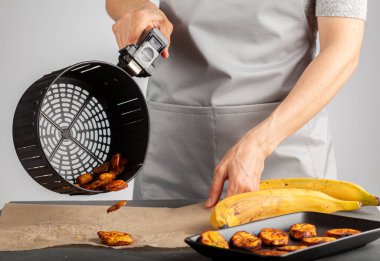 Beyaz bir kadın taze yapılmış muz cipslerini (Platanos Maduros) soğutmak için pişirme kağıdına döküyor. Kızartma sepetinin sapını tutuyor. Kızartma makinesi normal kaloriye kıyasla düşük kalori üretiyor..