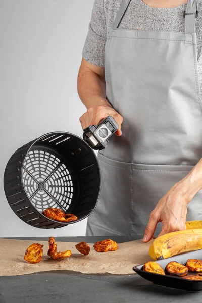 Beyaz bir kadın taze yapılmış muz cipslerini (Platanos Maduros) soğutmak için pişirme kağıdına döküyor. Kızartma sepetinin sapını tutuyor. Kızartma makinesi normal kaloriye kıyasla düşük kalori üretiyor..