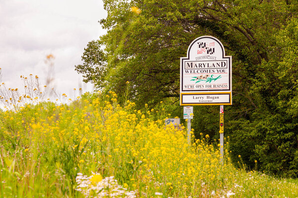  Maryland Welcomes You road sign on the scenic byway US Route 15 at the border of Maryland and Virginia.  It has MD flag and says open for business. Wildflowers in spring are all over the place