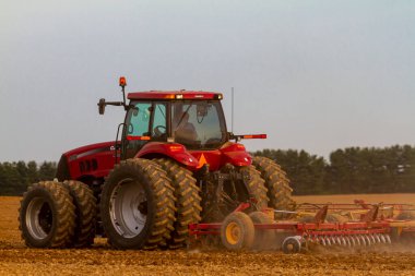Chestertown, MD, USA 05-02-2021: Kırmızı altı tekerlekli IH Magnum 305 model traktör ile kabin ilkbaharda boş bir tarla sürüyor. Saban eklentisi aracın arkasında toz bulutu oluşturuyor..