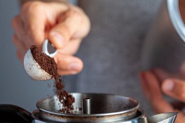 Kafkas bir kadın, plastik bir kaşık kullanarak kavanozdan bir çay kaşığı öğütülmüş kahve alıyor ve ev yapımı sabah kahvesi yapmak için bir kahve makinesine koyuyor. Seçici odak resmini kapat