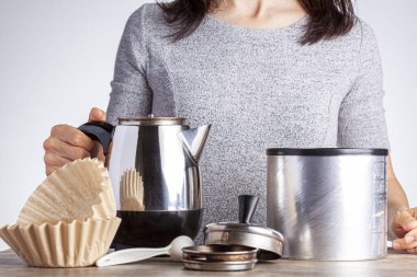 Kafkasyalı genç bir kadın kahve masasında kahve hazırlarken filtre kağıdı ve bir kavanoz kahve kullanıyor. Beyaz arka plana karşı. Ev yapımı sabah kahvesi..