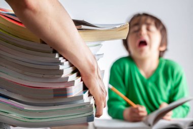 Çocuk konseptinden yüksek akademik başarı beklentileri olan hırslı ebeveynlik. Bir anne, ödevlerini yaparken ağlayan ve protesto eden sıkılmış, yorgun çocuğuna bir yığın test kitabı getiriyor.