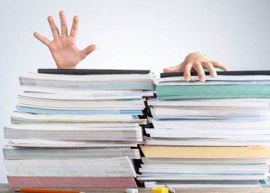 Genç bir öğrenciyi çalışma masasındaki büyük bir test kitaplarının arkasında gösteren soyut bir konsept resim. Ezici bir yük. Çocuk boğuluyormuş gibi yığının üstüne tırmanarak kaçmaya çalışıyor.