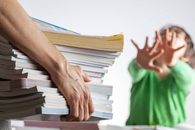 Çocuk konseptinden yüksek akademik başarı beklentileri olan hırslı ebeveynlik. Bir anne, hayır diyen ve ödevlerini protesto eden bezgin çocuğuna bir yığın test kitabı getiriyor..