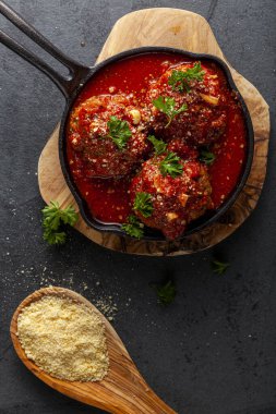 Dökme demir tavada cızırdayan domates soslu geleneksel İtalyan köftelerini yakından izleyin. Tava ahşap, maydanoz ve rendelenmiş parmesan peynirinin üzerine oturur.  