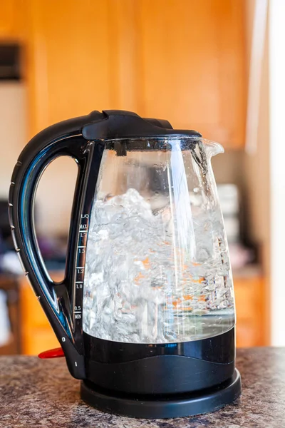 Boiling water in glass kettle on top of a kitchen counter with cabinets in background. Isolated versatile concept image for breakfast, morning, cooking, beverages, drinks, cooking etc.