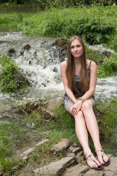 Menina bonita sentada ao lado de um riacho de montanha — Fotografia de Stock