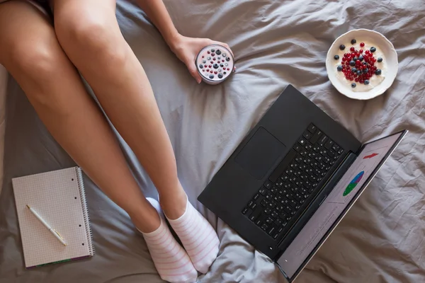 Frauenfüße, Laptop, Joghurt und Notizbuch auf der grauen Decke — Stockfoto
