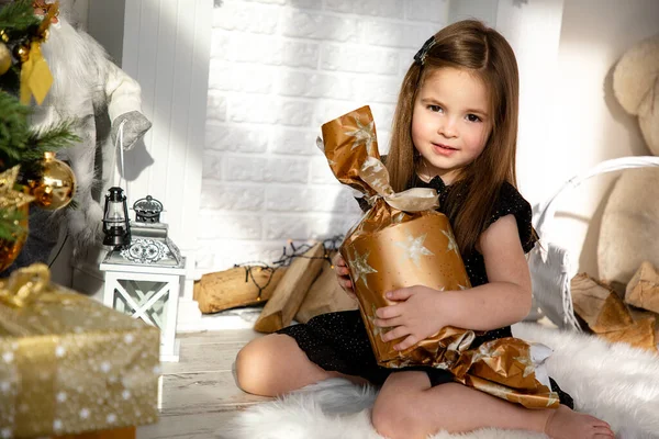 Cute little girl z pudełka z prezentem zabawy w pobliżu choinki wewnątrz. Wesołych Świąt i Szczęśliwego Nowego Roku — Zdjęcie stockowe