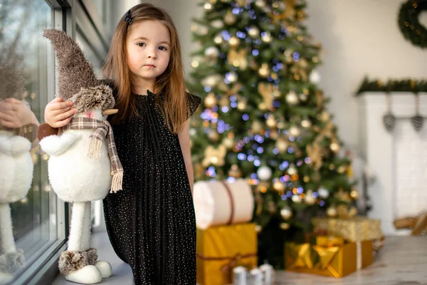 Cute little girl z bałwana zabawy w pobliżu choinki wewnątrz. Wesołych Świąt i Szczęśliwego Nowego Roku — Zdjęcie stockowe