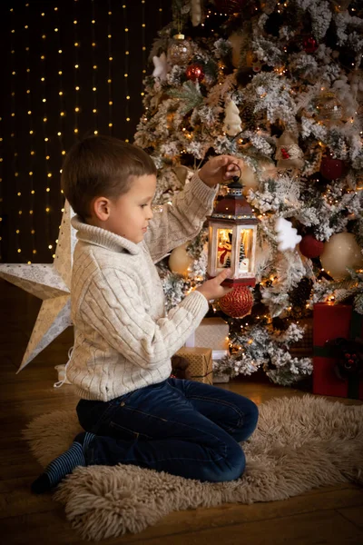 Petit garçon tenant une lanterne blanche dans sa main et assis près du sapin de Noël, Bonne année — Photo