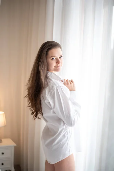 Brunette in mens shirt. Rear view of young woman looking through the window — Stock Photo, Image