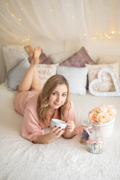 Chica joven sexy acostada en la cama blanca con flores - regalo para el 14 de febrero o el 8 de marzo — Foto de Stock