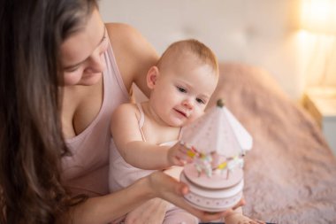 Genç, güzel bir anne ve küçük kızı yatak odasında el yapımı tahta oyuncaklarla oynuyorlar.