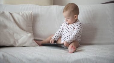 Küçük kız beyaz koltukta oturuyor ve elinde tablet var.