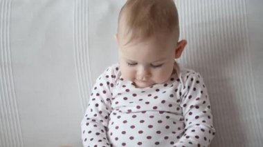 Kanepede oturan ve kolunu sallayan tatlı bir kız bebek, ağır çekim video.