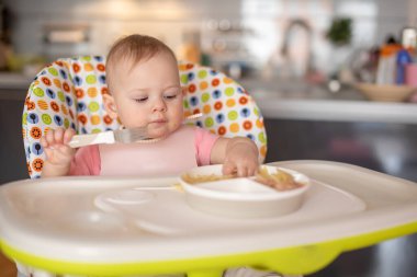 One year old girl having balanced meal in baby eating chair, healthy balanced nutrition for child