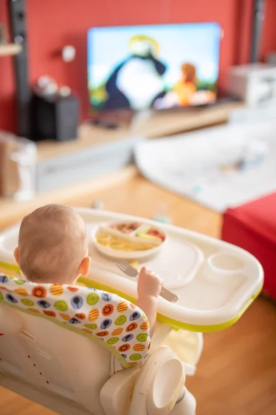 Baby girl watching cartoons on TV and eating balanced meal