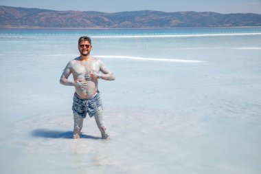 Mutlu ve komik erkek turist doğal kozmetik kilini Salda Gölü, Türkiye 'de vücuduna sürdü