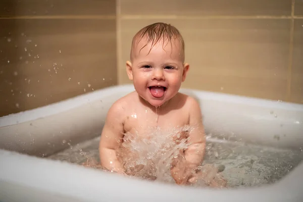 Liten charmig flicka babe leker i vattnet i små uppblåsbara baby pool som ligger i duschkabinen i badrummet, liten flicka ler och har kul — Stockfoto