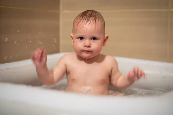 Liten charmig flicka babe leker i vattnet i små uppblåsbara baby pool som ligger i duschkabinen i badrummet, liten flicka ler och har kul — Stockfoto
