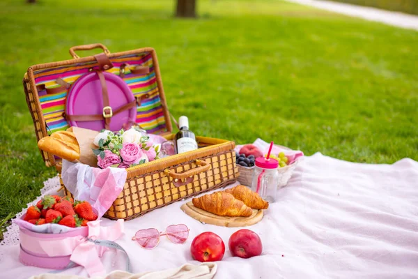 Picnic in the park under blooming cherry trees with fruit, wine and croissants