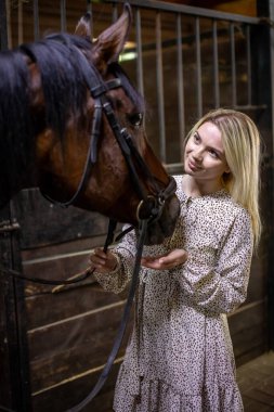 Uzun saçlı, sarışın genç bir kadın. Ahırda kahverengi atıyla poz veriyor. Rusya, Sibirya 'da.