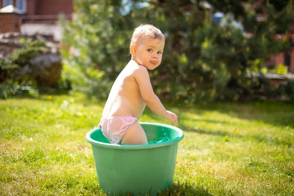 Baby flicka flopp i ett handfat med vatten på hemmaplan på sommaren — Stockfoto
