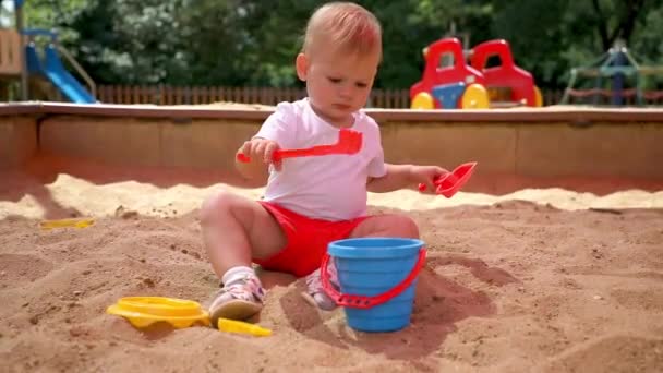 Liebenswertes Kleinkind spielt mit Sand auf Sandkasten auf Spielplatz — Stockvideo
