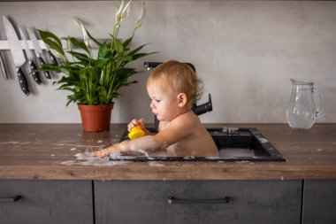 Evdeki mutfak lavabosunda su ve köpükle oynayan tatlı, mutlu bir kız.