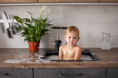 Evdeki mutfak lavabosunda su ve köpükle oynayan tatlı, mutlu bir kız.