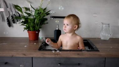 Evdeki mutfak lavabosunda su ve köpükle oynayan tatlı, mutlu bir kız.