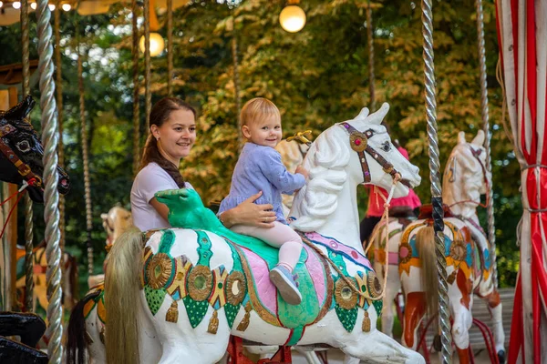 Cute baby girl with mother on the horse of old retro carousel, Prague, Czech republic — Stock Photo, Image