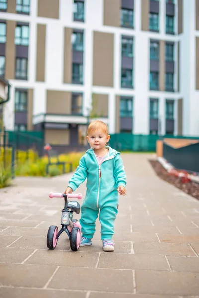 Cute little toddler girl in blue overalls riding on run balance bike. Happy healthy lovely baby child having fun with learning on leaner bicycle. Active kid on cold day outdoors. — Stock Photo, Image