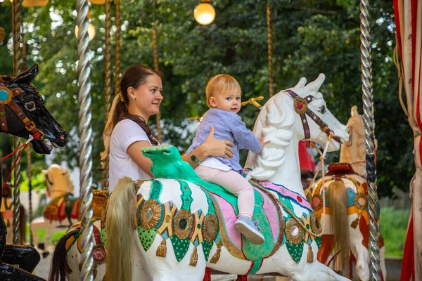 Cute baby girl with mother on the horse of old retro carousel, Prague, Czech republic — Stock Photo, Image