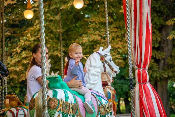 Cute baby girl with mother on the horse of old retro carousel, Prague, Czech republic — Stock Photo, Image