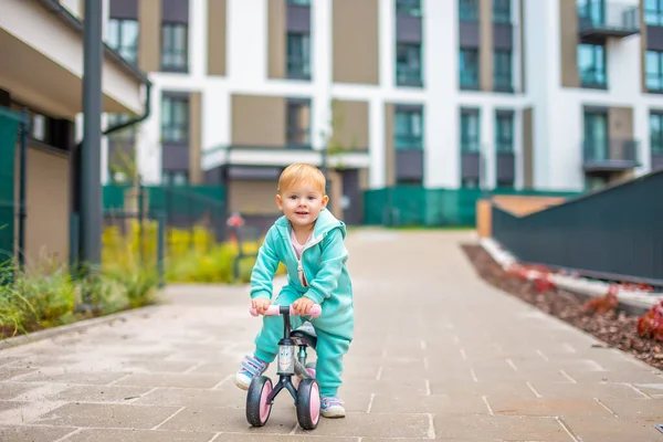 Cute little toddler girl in blue overalls riding on run balance bike. Happy healthy lovely baby child having fun with learning on leaner bicycle. Active kid on cold day outdoors. — Stock Photo, Image